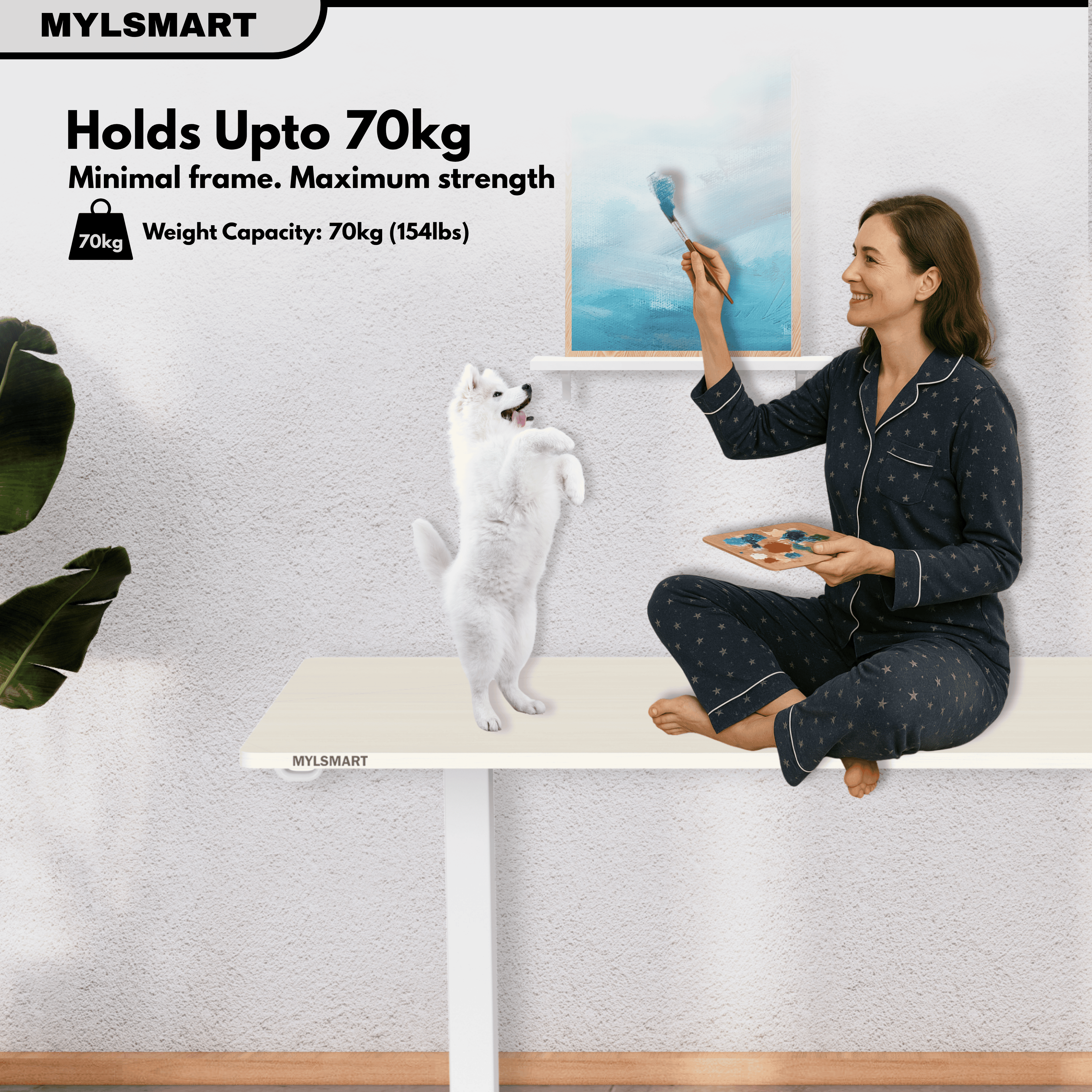 Woman sitting on a strong and sturdy Mylsmart standing desk with a dog, holding a paint brush, against a light grey wall.